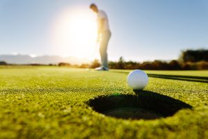 Pro golfer putting golf ball in to the hole. Golf ball by the hole with player in background on a sunny day.